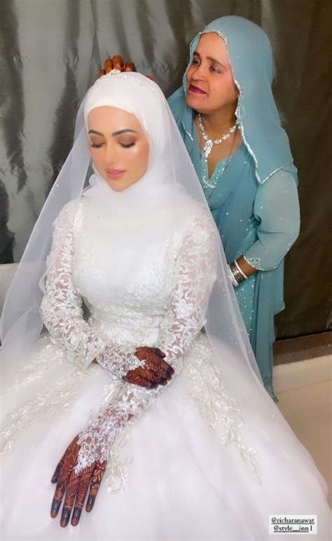 two women dressed in wedding attire and one is wearing a white dress with brown gloves