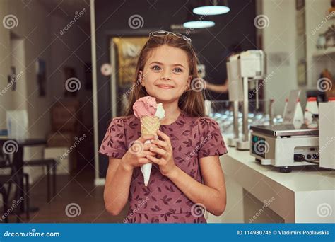 Beauty Little Girl in a Fashionable Dress Eating Strawberry, Standing in an Ice Cream Parlor ...