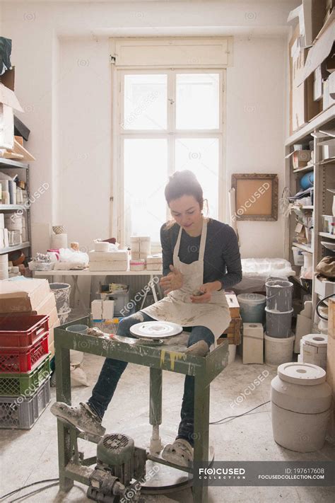 Caucasian woman is shaping pottery clay on a pottery wheel in a ceramic workshop. — inside ...