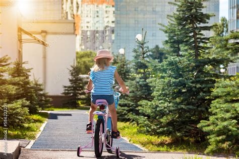 Back view of little child in pink hat riding bike in summer park ...