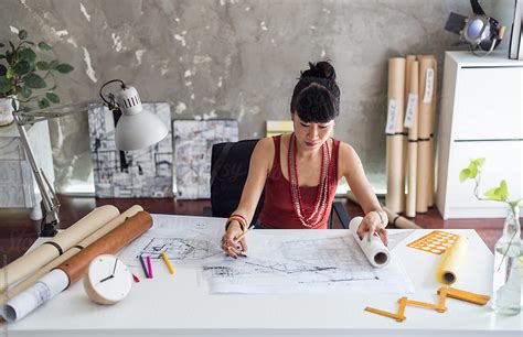 "Female Architect Working On Blueprints At Desk" by Stocksy Contributor "Jovo Jovanovic" - Stocksy