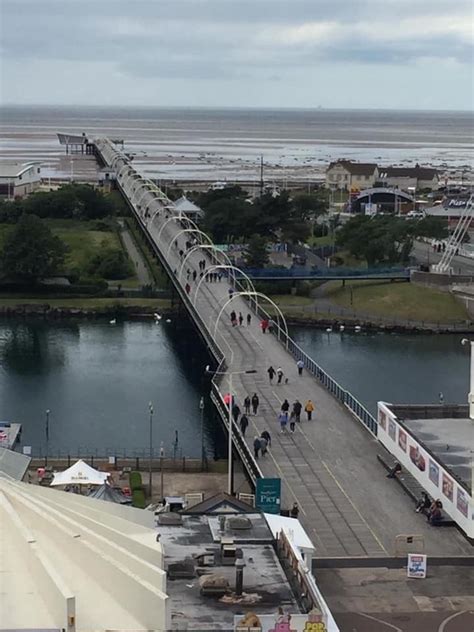 people walking across a bridge over a river next to a beach and ocean ...