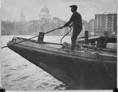 A lighterman standing on the bow of a lighter, hauling on a rope. | Royal Museums Greenwich