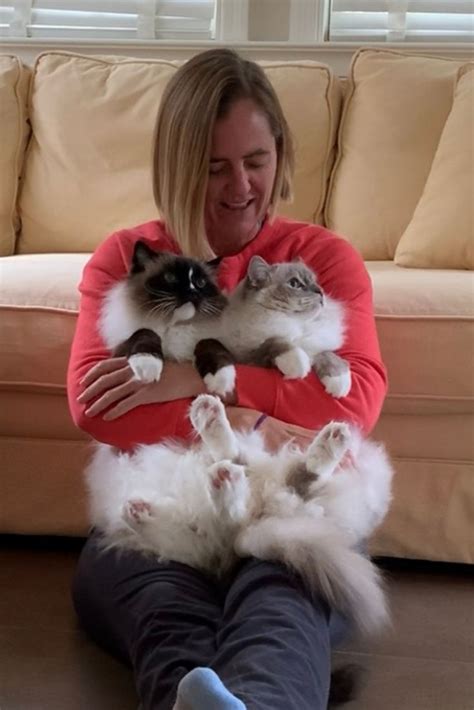 a woman sitting on the floor holding two cats