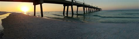 the sun is setting over the ocean with a pier in the background