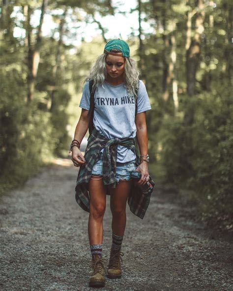 a woman walking down a dirt road in the woods wearing a t - shirt and shorts