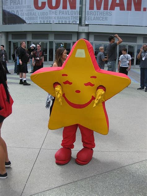 a person dressed as a star standing in front of a building with people walking around