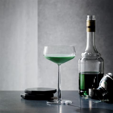 a green liquid in a wine glass next to a bottle and coaster on a table