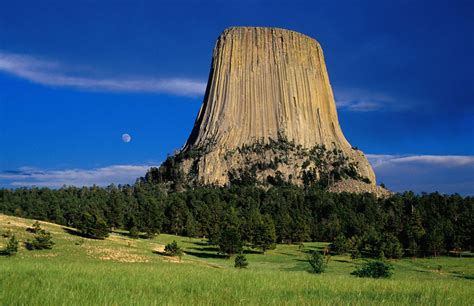 a tall rock formation towering over a lush green field under a blue sky ...