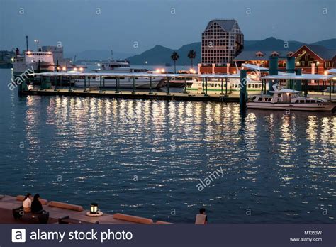 View of Sasebo, Japan by the sea with boats docked and people relaxing, looking at the water. It ...