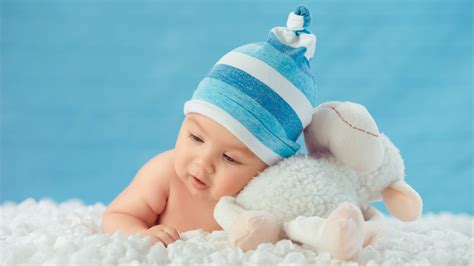 Beautiful Cute Baby Is Lying Down On White Cloth Wearing Blue And White Cap With Bunny Aside In ...