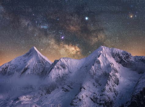 Amazing view of white snowy mountain range under incredible night starry sky with breaking rays ...