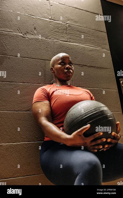 Focused female athlete doing wall sit exercise with medicine ball at ...