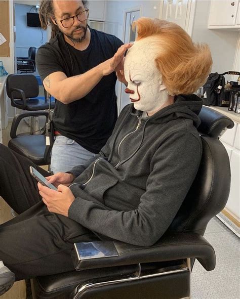 a man with red hair sitting in a chair next to a woman who is using a cell phone