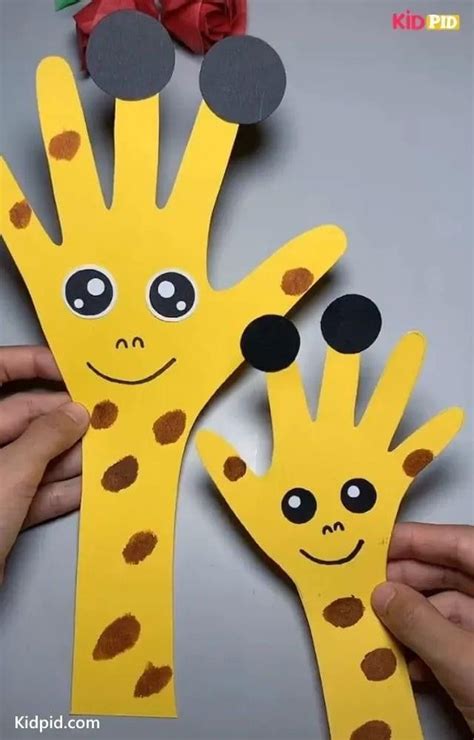 two hands holding up paper cut out to look like giraffes with faces on them