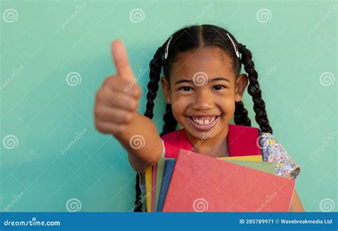 Portrait of Happy Biracial Schoolgirl with Thumb Up Over Blue Background at Elementary School ...