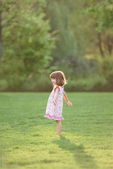 «Little Girl Wearing White Dress Standing Barefoot In The Grass» del colaborador de Stocksy ...