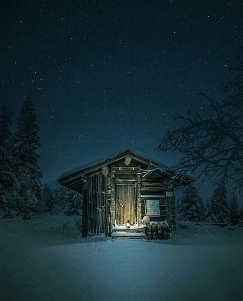 a cabin in the snow at night with lights on and stars above it's roof