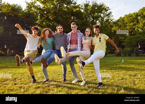 Funny group of friends having fun and fooling around dancing cancan in park on green lawn Stock ...