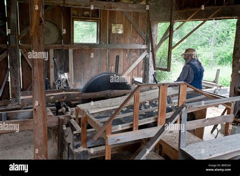 Lumbermill worker squares a log. A lumber mill worker uses a large saw to strip the bark from a ...