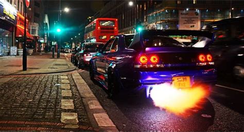 the back end of a car on a city street at night with traffic passing by