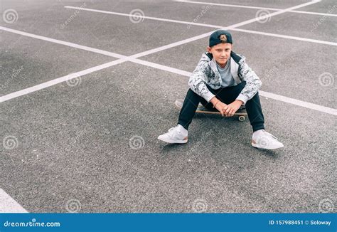 Teenager Skateboarder Boy with a Skateboard Sitting on Asphalt Playground and Resting after he ...