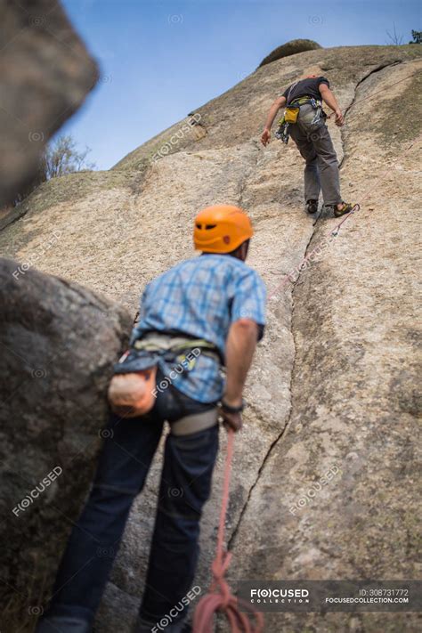 Adventurers climbing mountain wearing safety harness against picturesque landscape — active ...