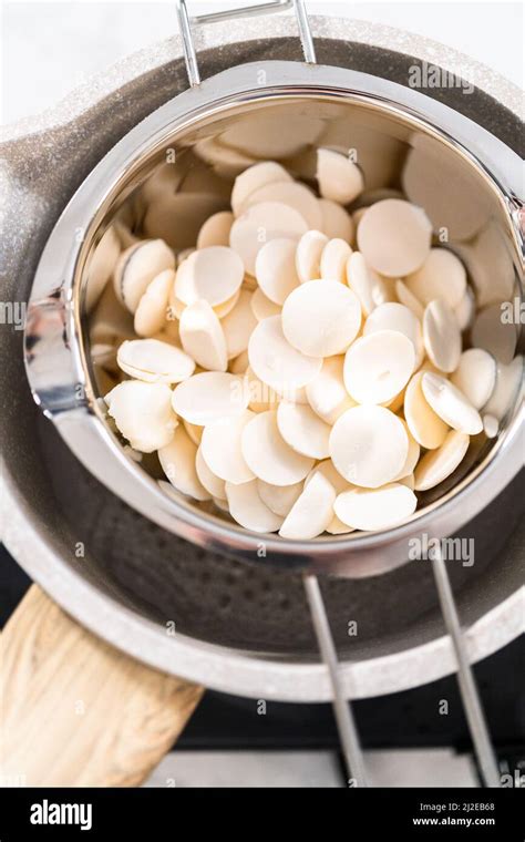 Melting white chocolate chips in a stainless steel double boiler pot over a cooking pot with hot ...