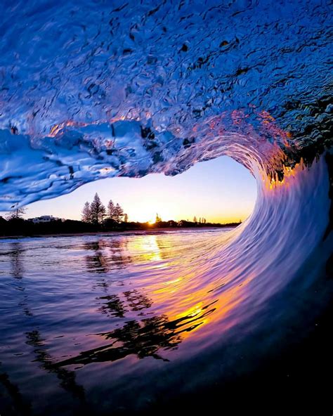 an ocean wave with the sun setting in the background