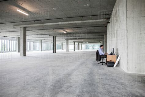 Businessman sitting at a small desk in a large empty raw office space. - Stock Photo - Dissolve