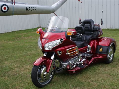 a red motorcycle parked on top of a lush green field next to a plane ...