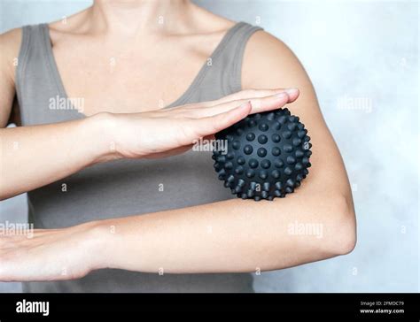 A young woman massages her elbow with spiky trigger point ball, tennis ...