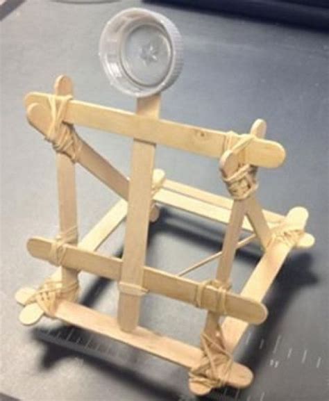 A photograph shows a small catapult structure made from Popsicle sticks ...