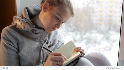 Young Girl Writing In Her Journal While Sitting At A Large Window Stock video footage | 1763468