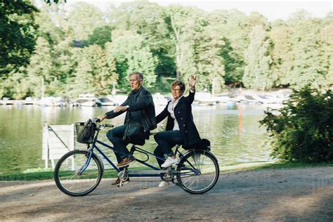 Senior couple enjoying tandem bike ride by pond in park - Stock Photo ...