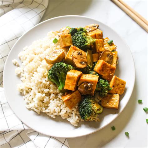 a white plate topped with tofu and broccoli next to chopsticks