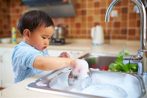 "One Lovely Kid Wash The Dishes In The Kitchen" by Stocksy Contributor "Bo Bo" - Stocksy