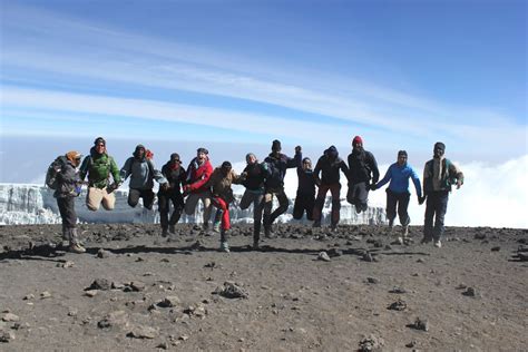 A multicultural team celebrating at the summit of Mount Kilimanjaro who ...