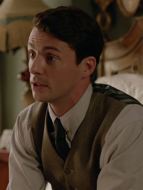 a man in a vest and tie sitting on a bed looking off to the side