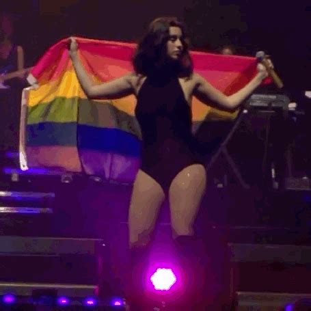 a woman in black dress on stage holding a rainbow flag