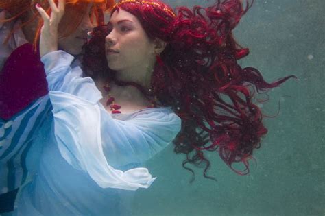 a woman with red hair is under water holding an orange object in her ...