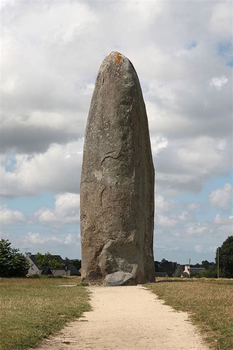 a large rock sitting in the middle of a field next to a dirt path and trees