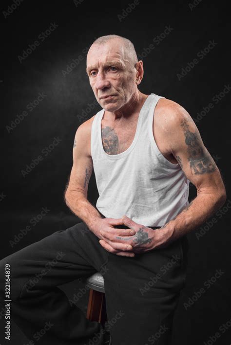 Old man with tattoos is sitting on a chair. Stock Photo | Adobe Stock