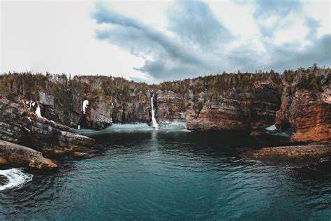 Rocky ravine with waterfall flowing into blue sea · Free Stock Photo