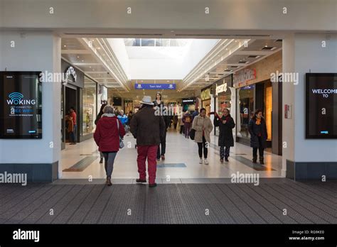 People (shoppers) going in and out of Peacocks shopping centre, an indoor mall in Woking town ...