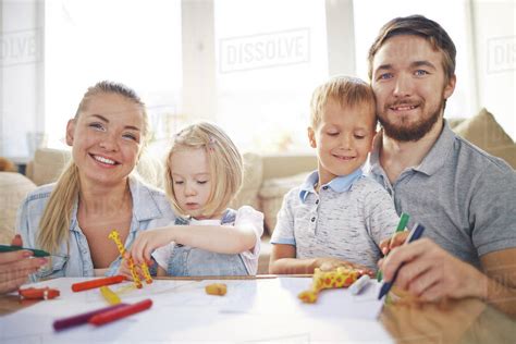 Young married couple drawing with their two kids, enjoying time together and looking at camera ...