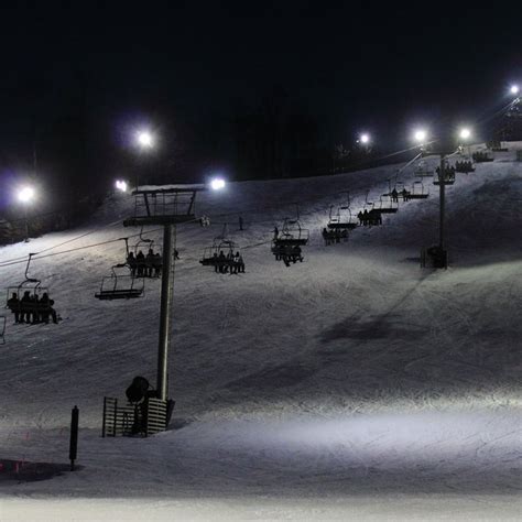 a ski slope at night with many people on the chairlifts and snowboarders