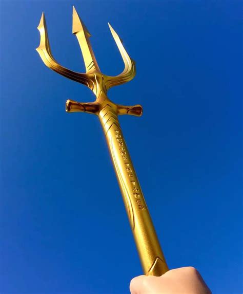 a hand holding a gold colored metal object in the shape of a large, pointed hammer