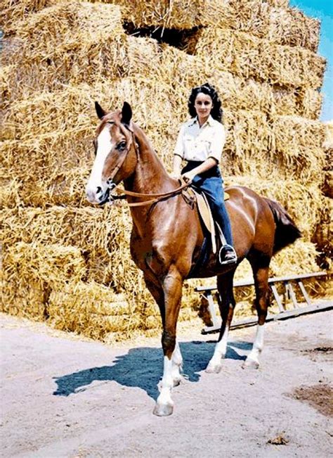 a woman riding on the back of a brown horse next to a pile of hay