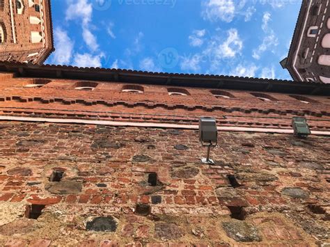 Old red brick wall and tiled roof of a medieval castle against the blue sky with white clouds ...